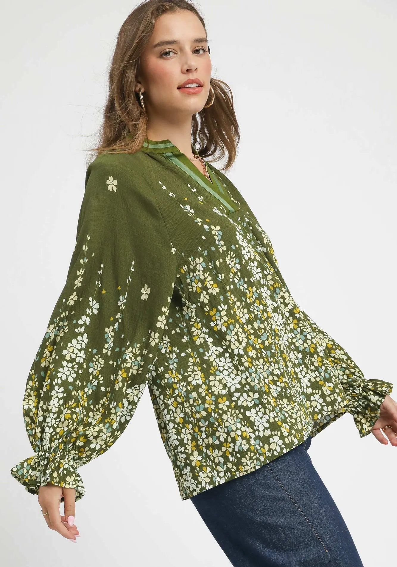 Woman wearing a green floral blouse with blue jeans on a white background
