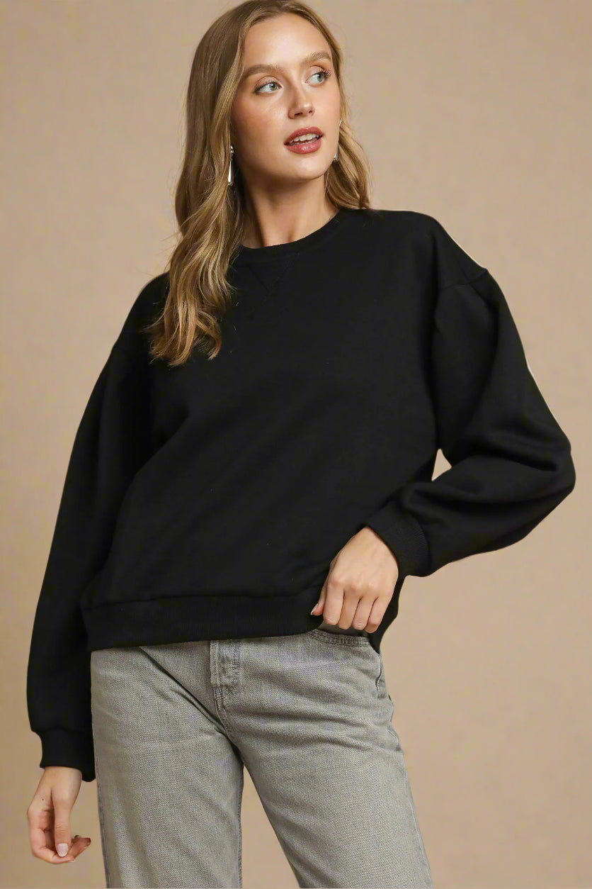 Woman wearing a black sweater and gray pants against a brown background
