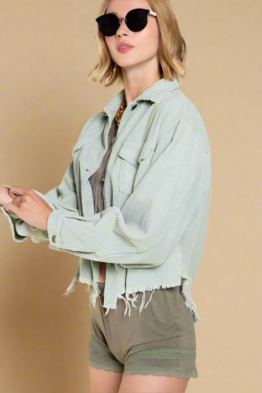 Woman wearing a light green jacket with frayed edges and beige shorts on a beige background