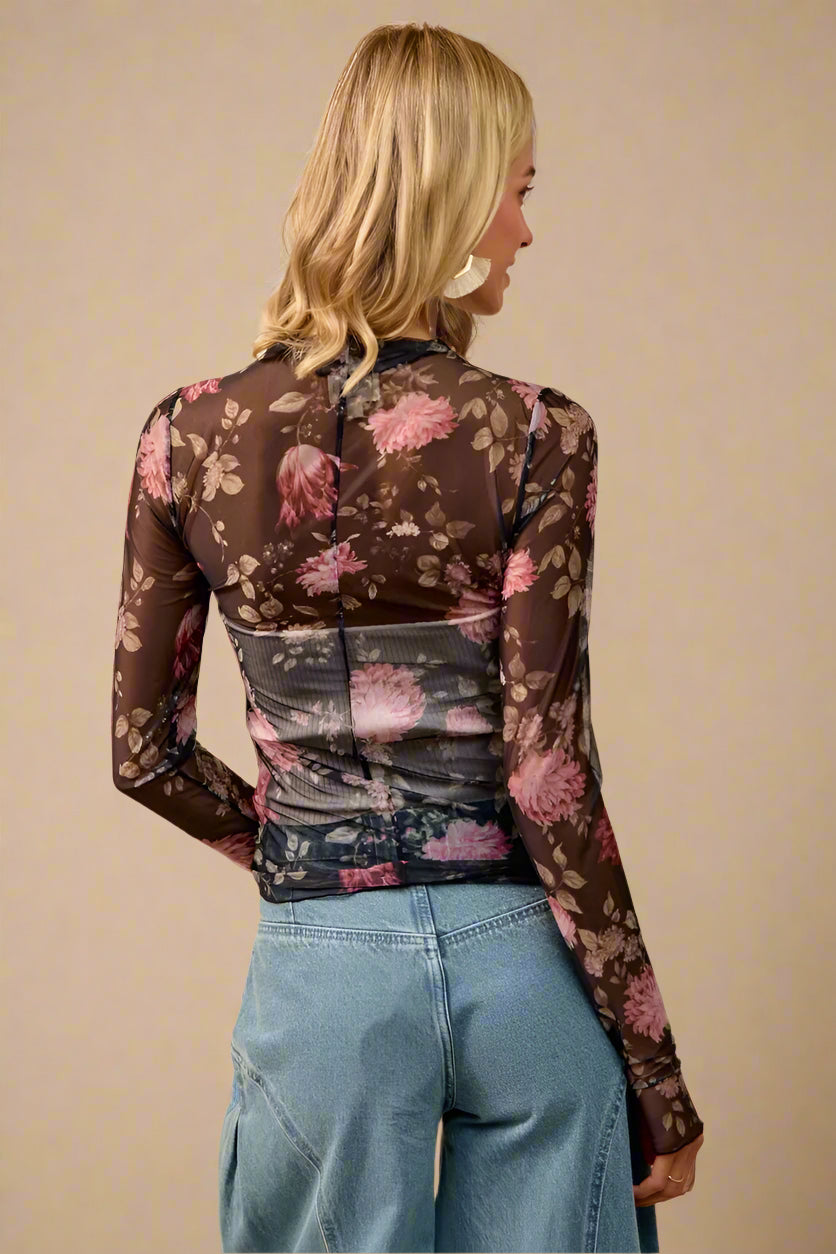 Woman wearing a floral sheer top with long sleeves against a beige background