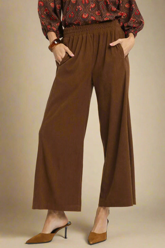 Brown wide-leg pants worn with a patterned top on a beige background