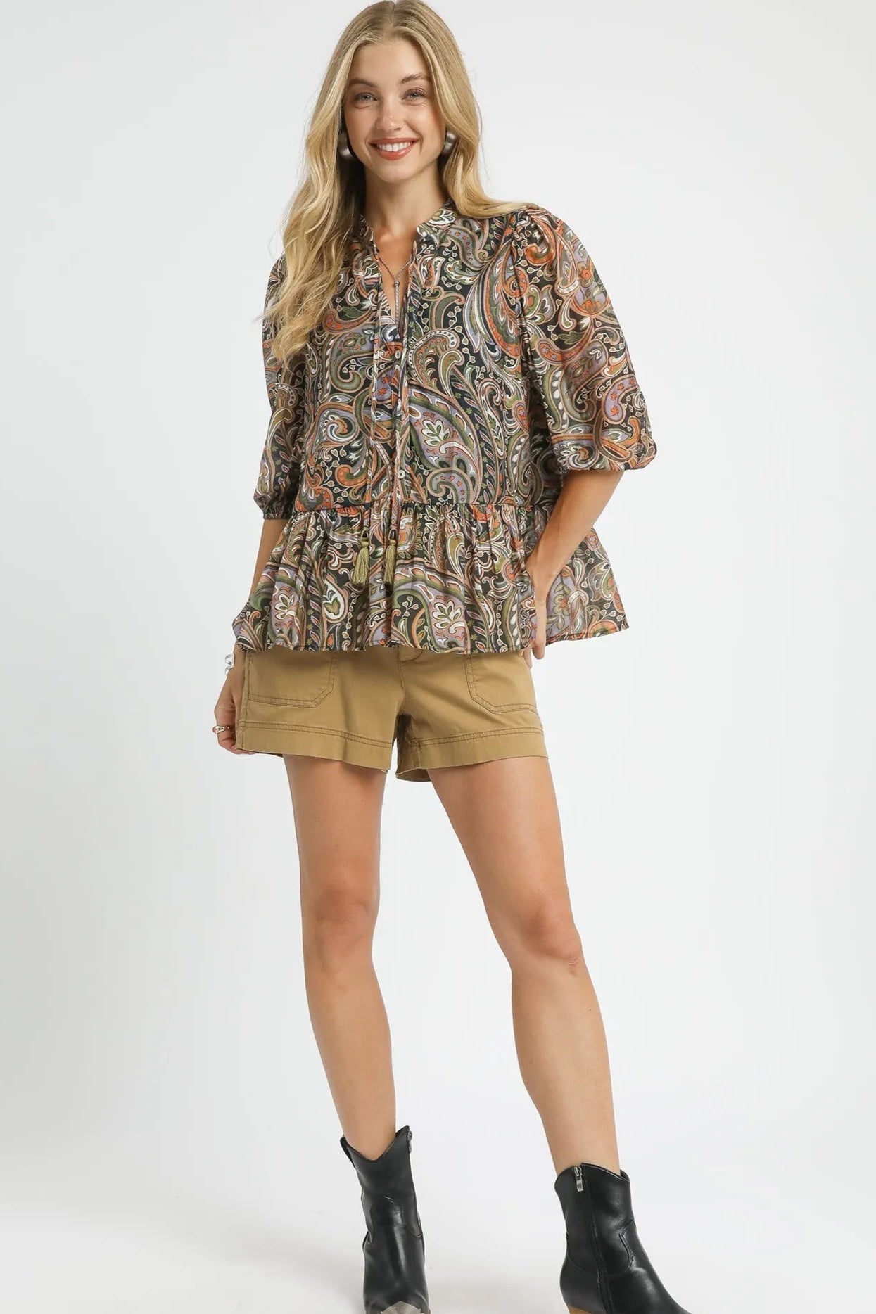 Woman wearing a patterned blouse, shorts, and boots on a white background
