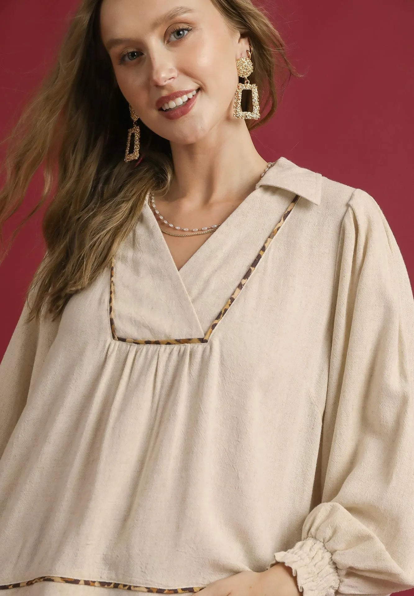 Woman wearing a beige blouse with decorative trim against a red background