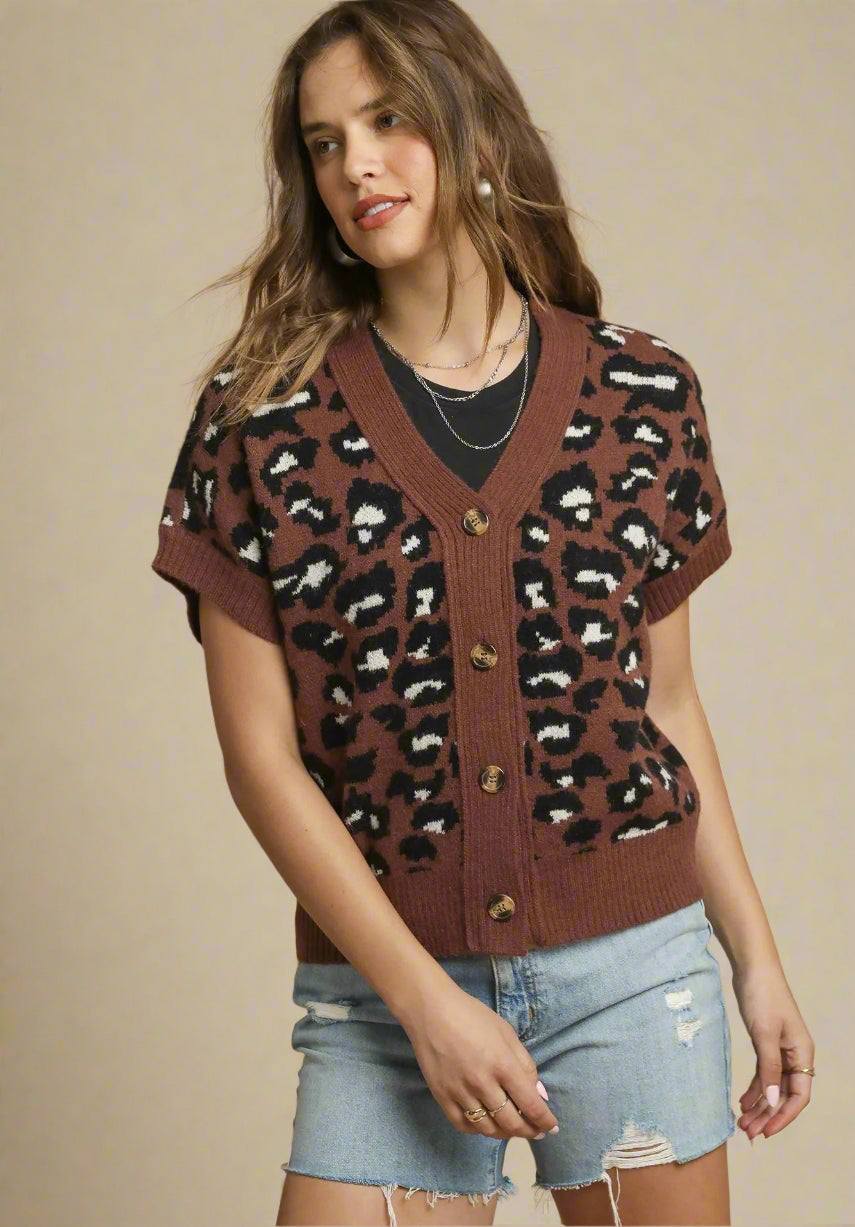 Woman wearing a brown leopard print cardigan with denim shorts on a beige background