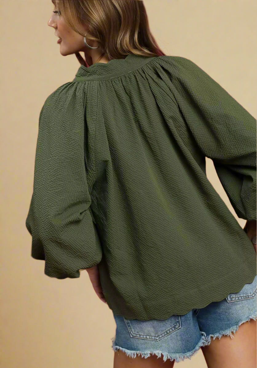 Person wearing an olive green blouse with long sleeves and denim shorts on a red background