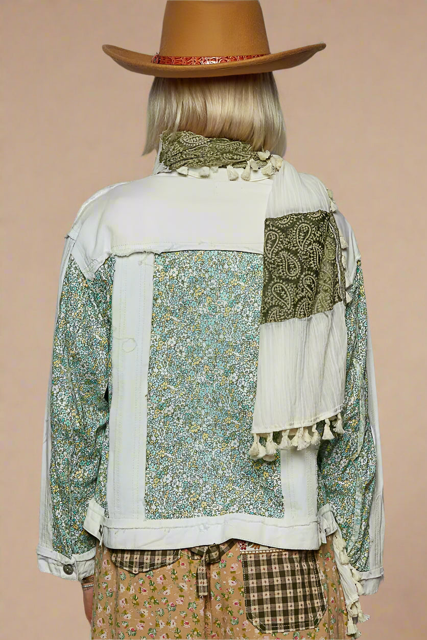 Person wearing a patchwork jacket with floral patterns and a brown hat on a gray background