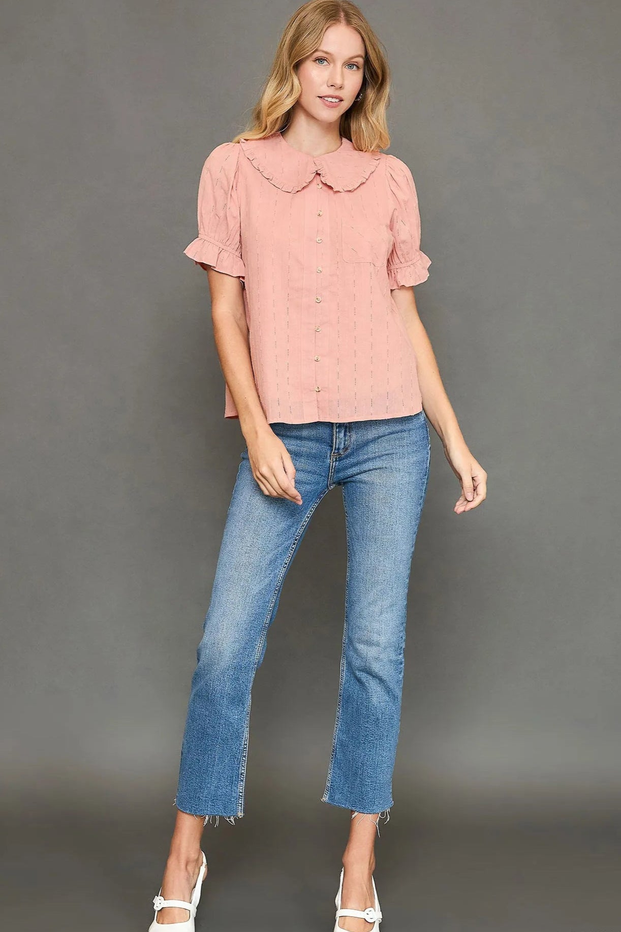 Woman wearing a pink blouse and blue jeans against a gray background