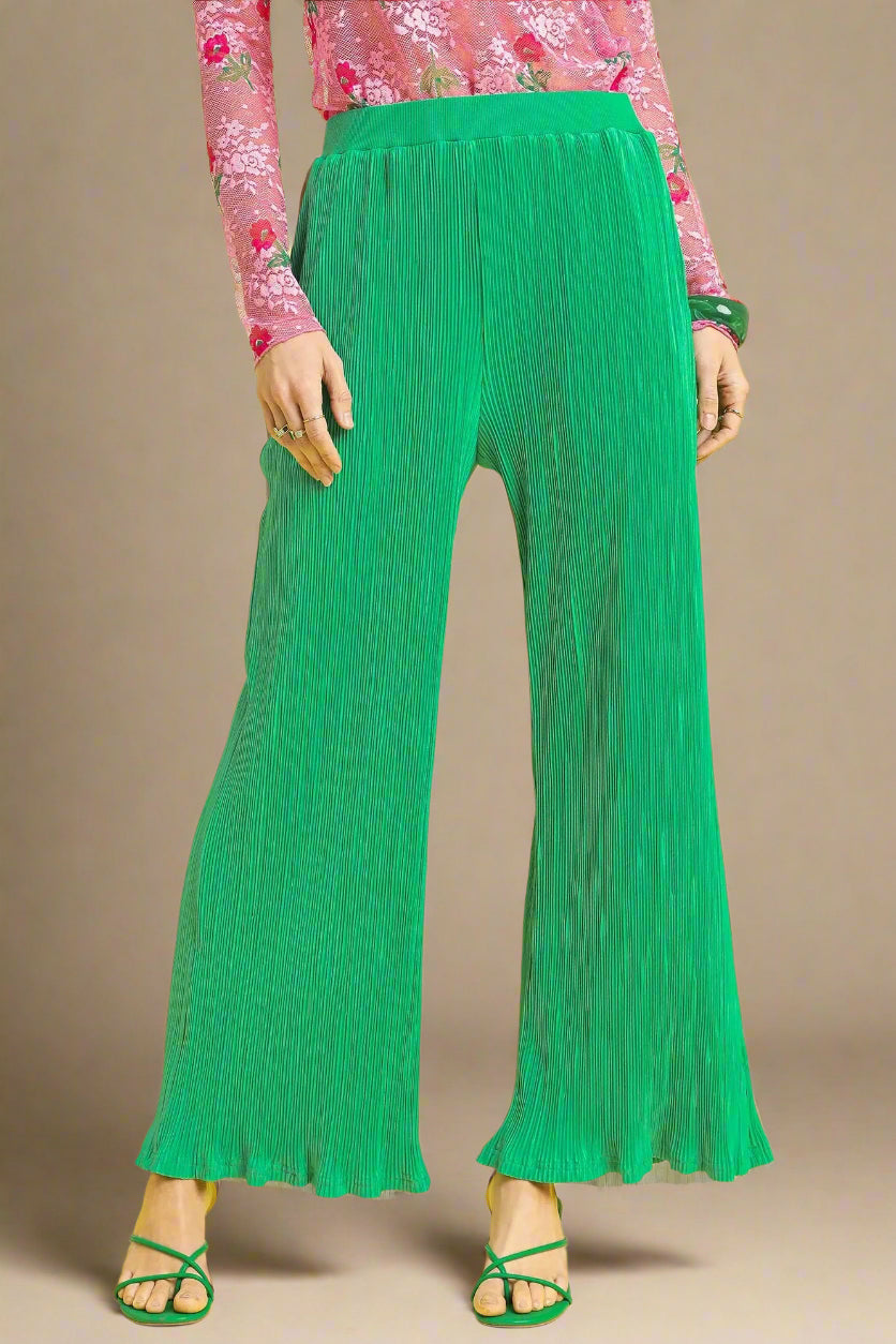 Green pleated pants worn with a pink floral top on a beige background
