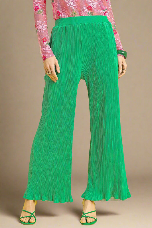 Green pleated pants worn with a pink floral top on a beige background