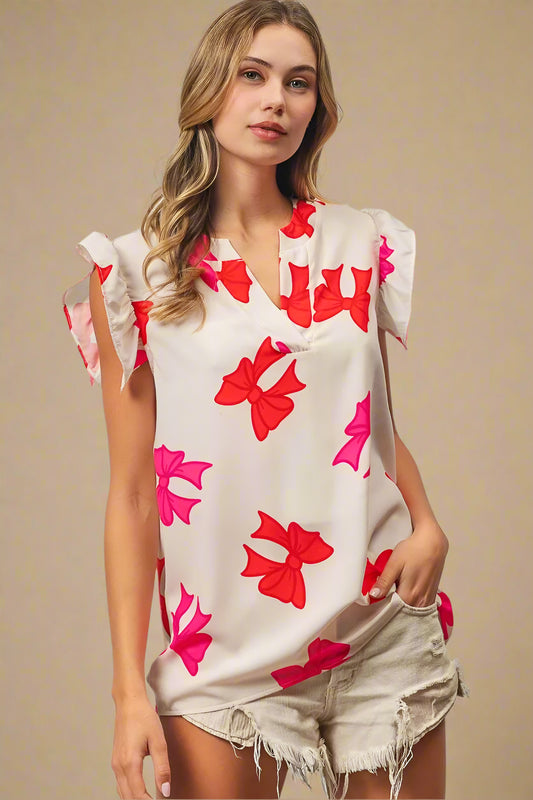 Woman wearing a white top with red and pink bow patterns against a light gray wall.