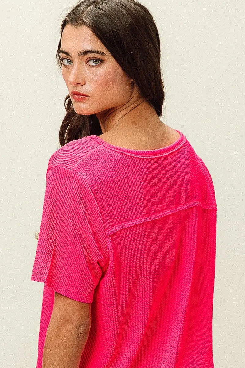 Woman wearing a bright pink textured top against a plain background