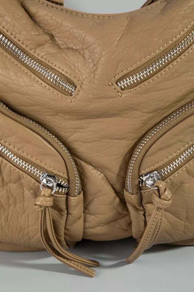 Close-up of a tan leather handbag with multiple zippers on a light gray background