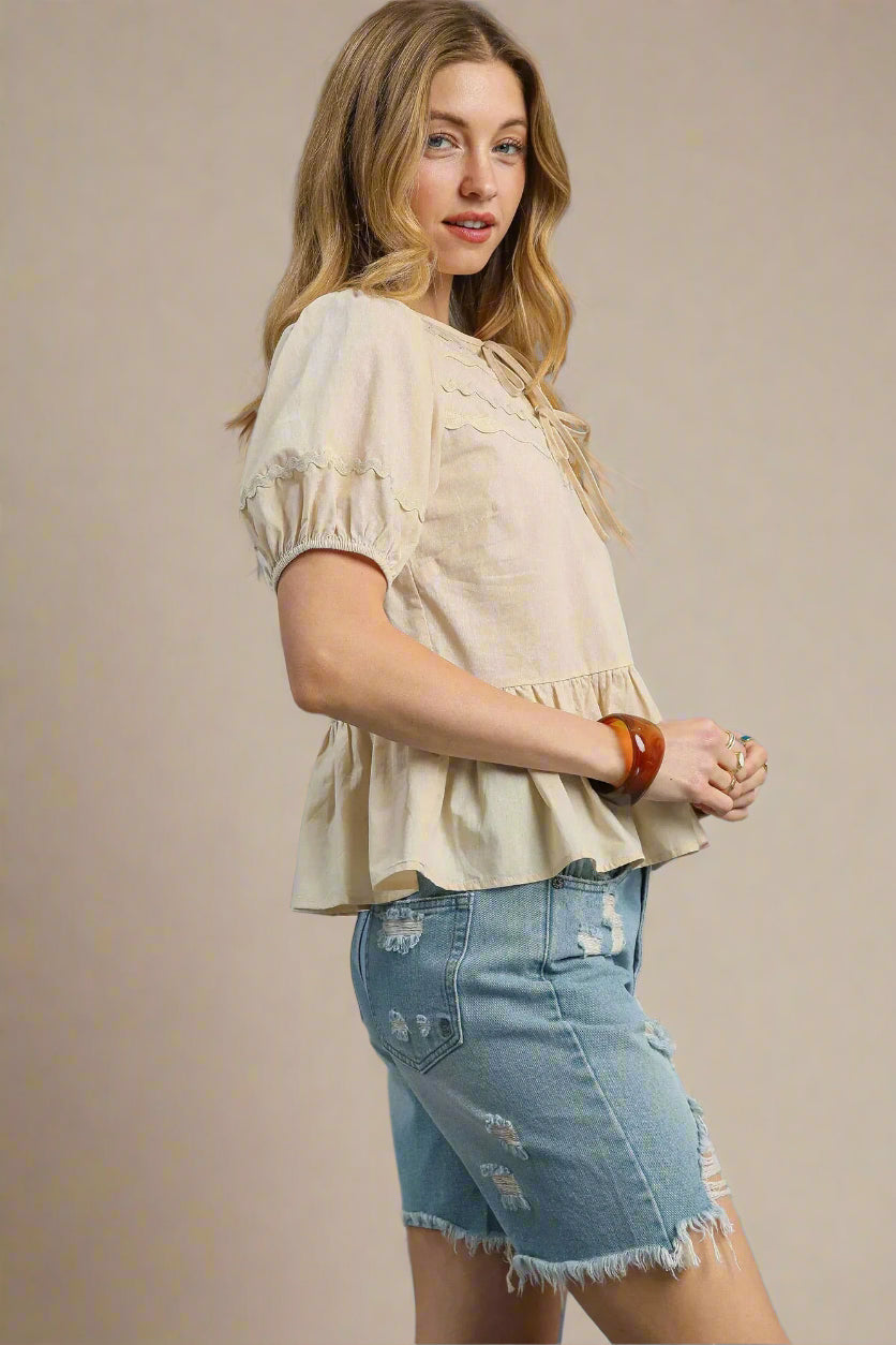 Woman wearing a beige blouse and denim shorts against a beige background