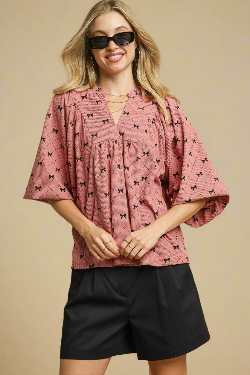 Woman wearing a pink blouse with black patterns and black shorts on a beige background