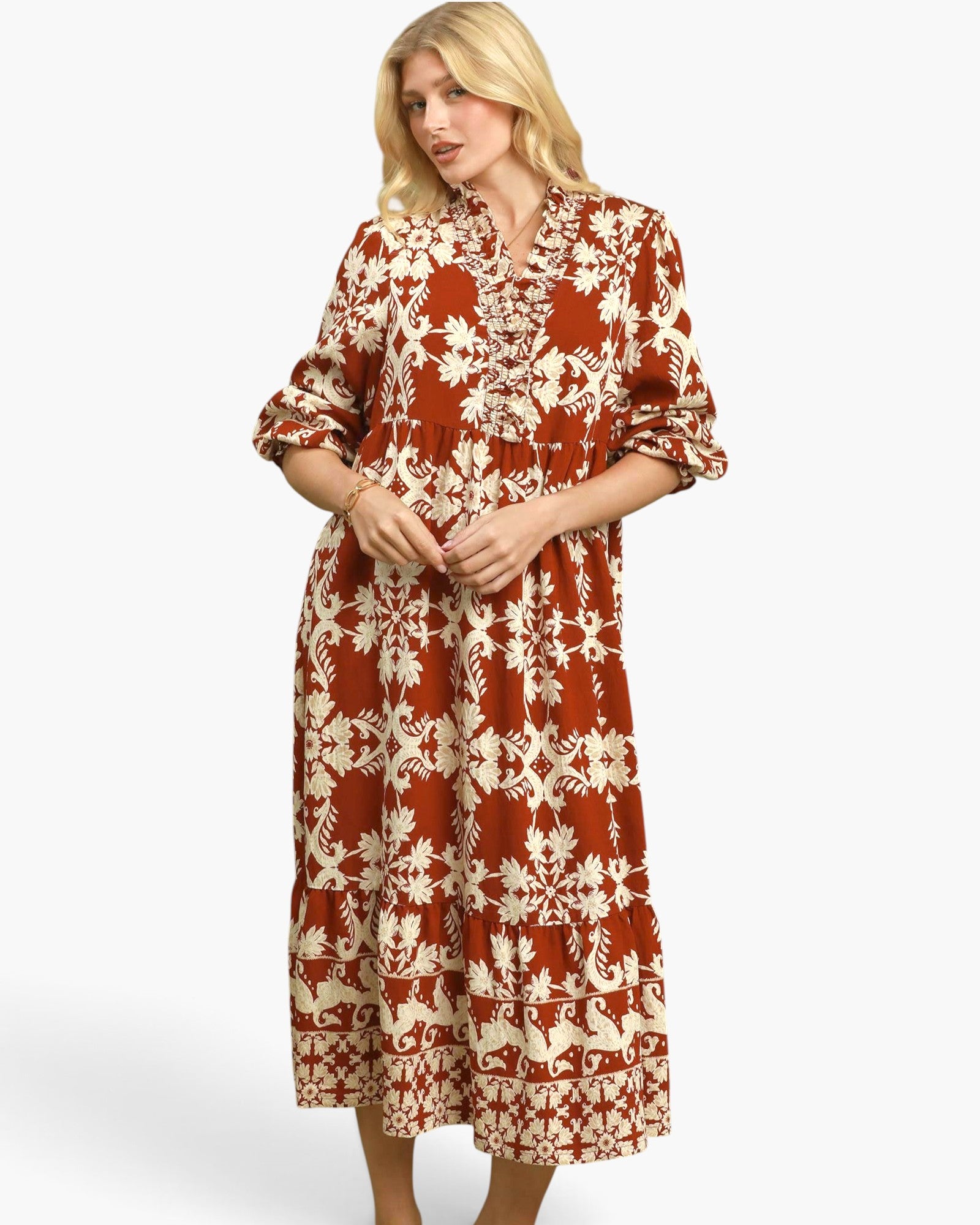 A woman modeling a rust-orange and cream patterned midi dress with three-quarter sleeves and a gathered waist, set against a plain light gray studio background.