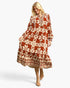 A woman modeling a long-sleeved midi dress with a rust orange and cream floral pattern, shown against a light gray studio background.