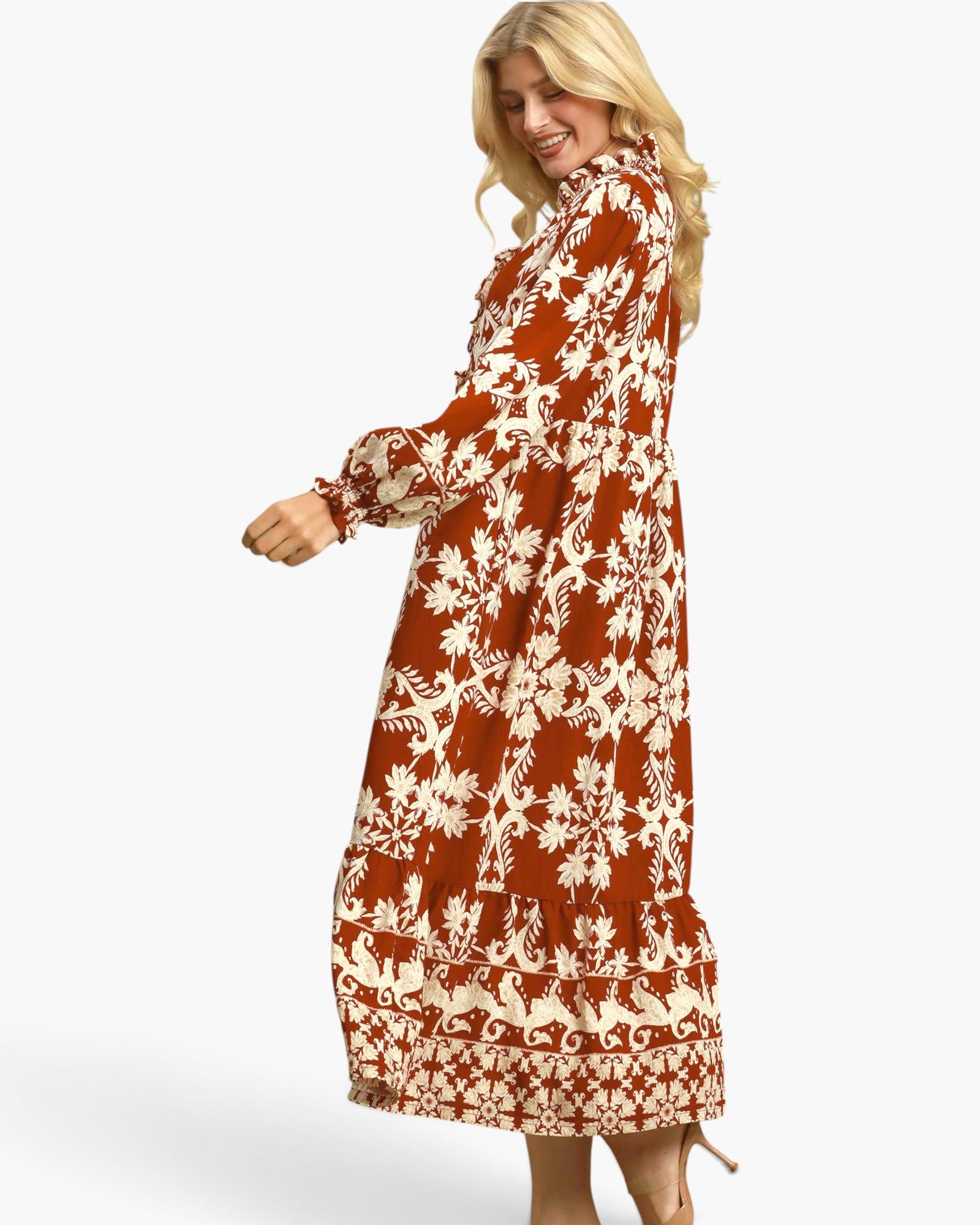 A woman modeling a long-sleeved midi dress with a rust-orange and cream floral pattern, shown from a side-back angle against a light gray studio background.