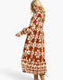 A woman modeling a long-sleeved midi dress with a rust-orange and cream floral pattern, shown from a side-back angle against a light gray studio background.
