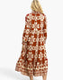 A woman shown from the back wearing a long-sleeve midi dress with a rust-orange and cream floral snowflake pattern, set against a plain white studio background.