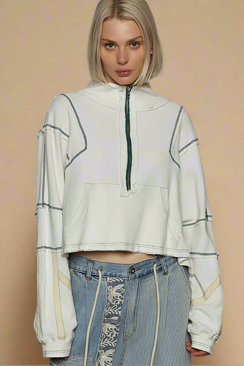 Person wearing a light-colored hoodie with a zipper and patterned jeans on a beige background