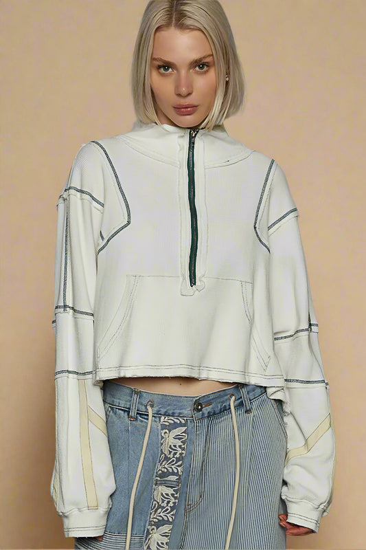 Person wearing a light-colored hoodie with a zipper and patterned jeans on a beige background