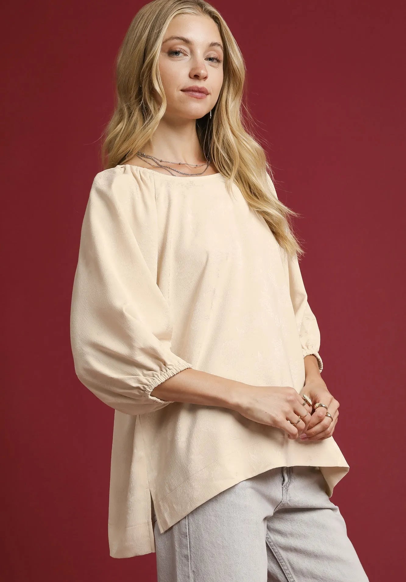 Woman wearing a beige blouse and light gray pants against a red background