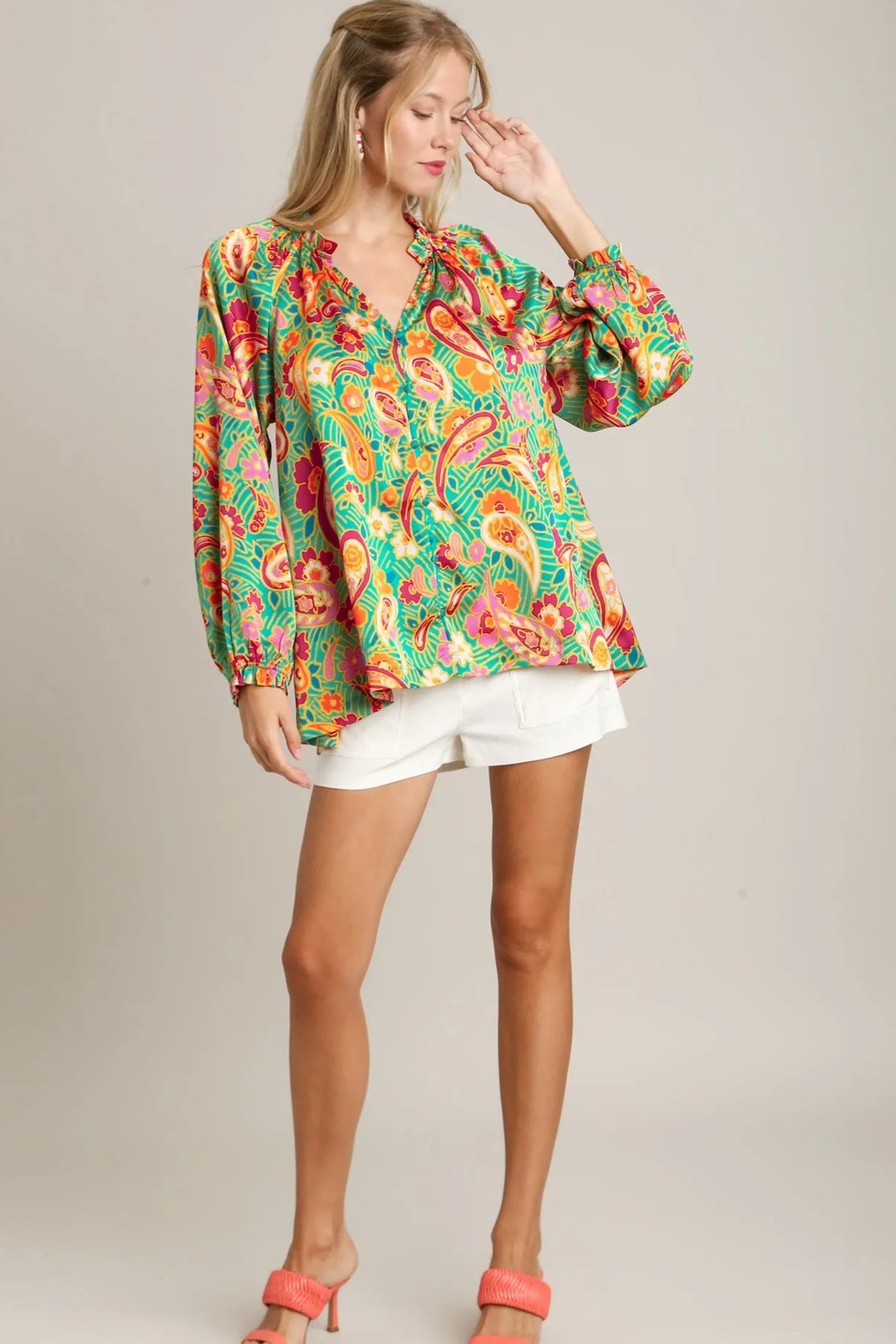 Woman wearing a colorful floral blouse and white shorts on a gray background