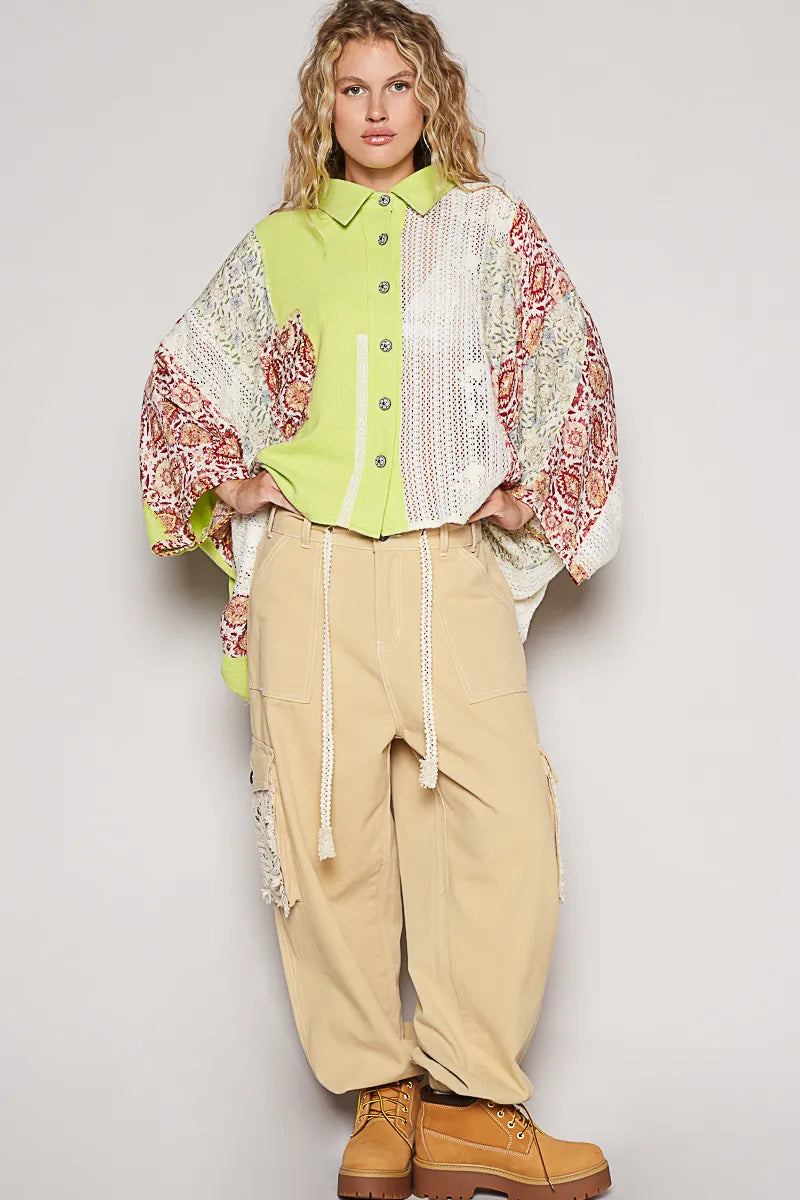 Woman wearing a colorful patterned jacket over a green shirt with beige pants against a plain background
