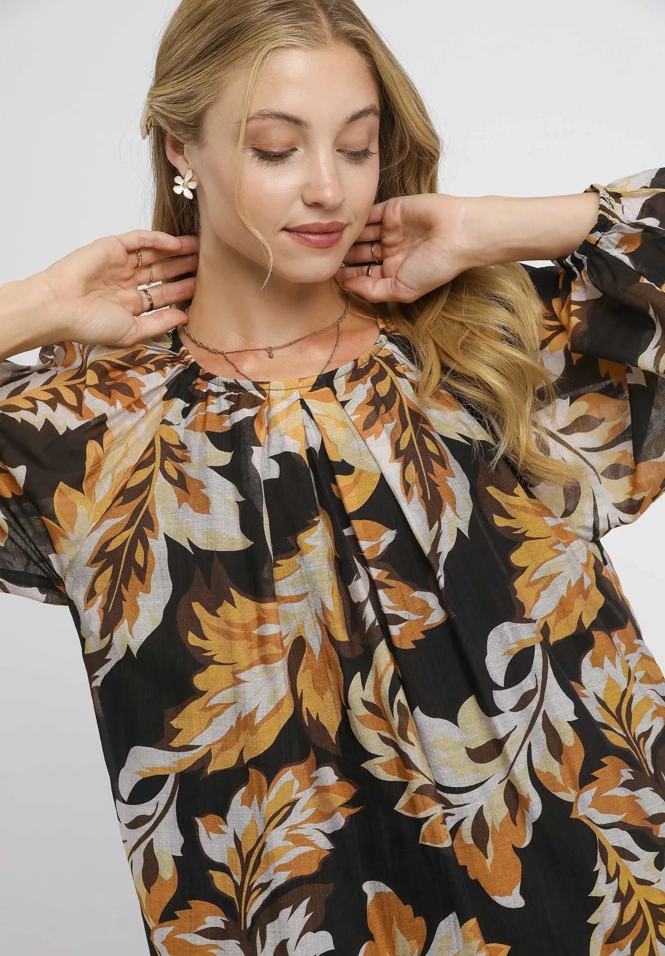 Woman wearing a black floral dress with gold and white patterns on a plain background