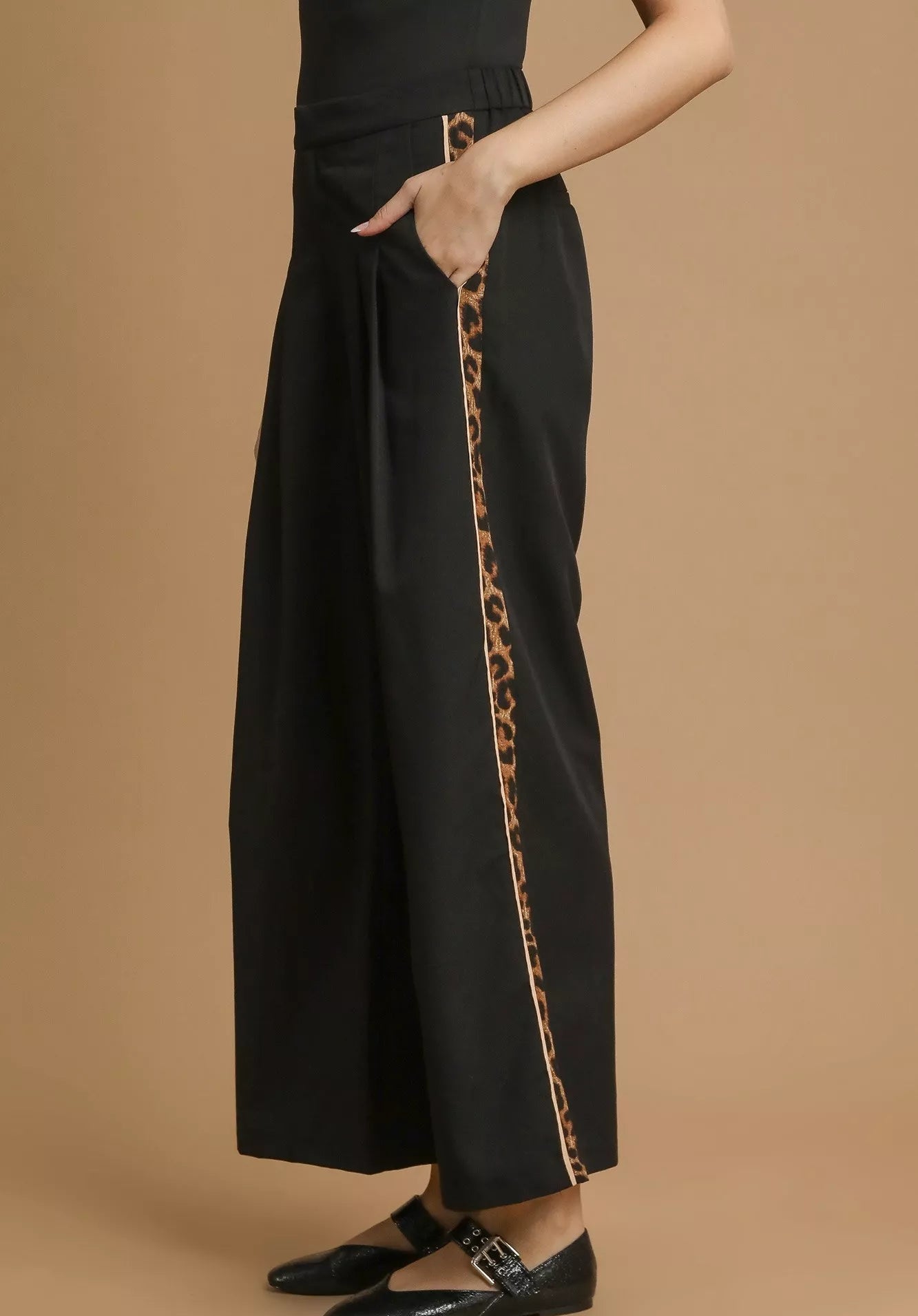 Black pants with a leopard print side stripe on a beige background