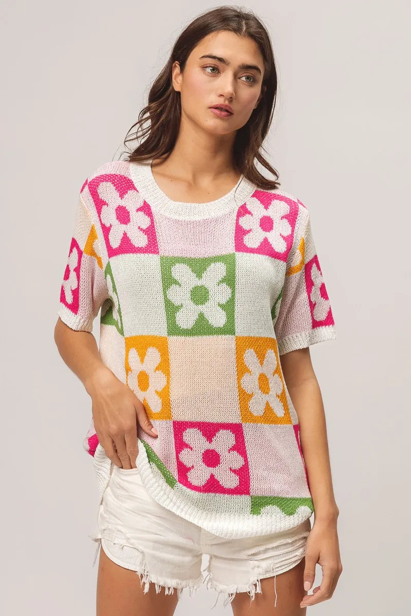 Woman wearing a colorful checkered sweater with flower patterns on a plain background