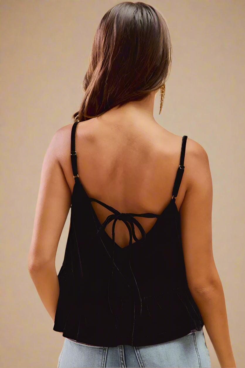 Woman wearing a black strappy top with a beige background