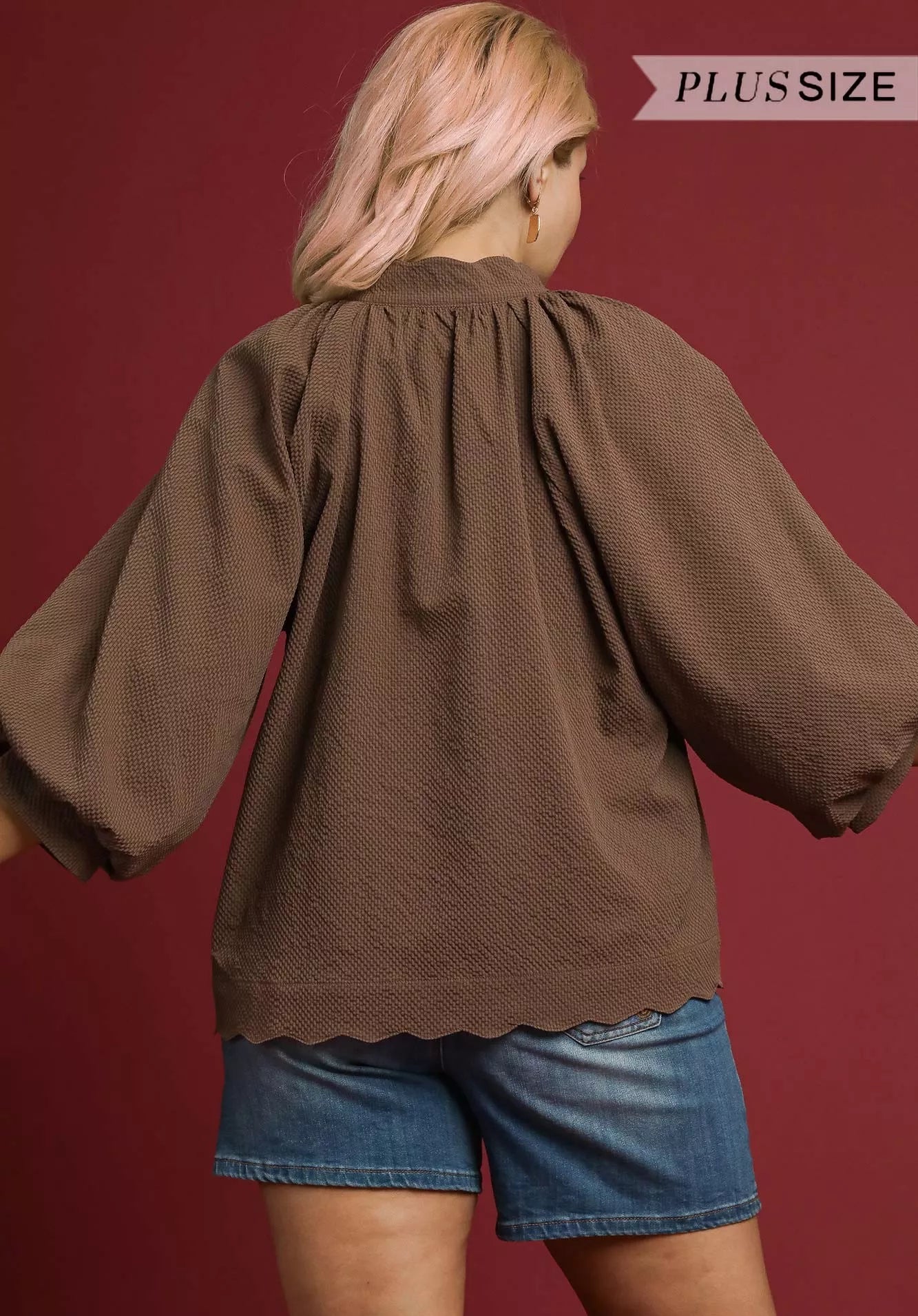 Woman wearing a brown blouse and denim shorts on a red background