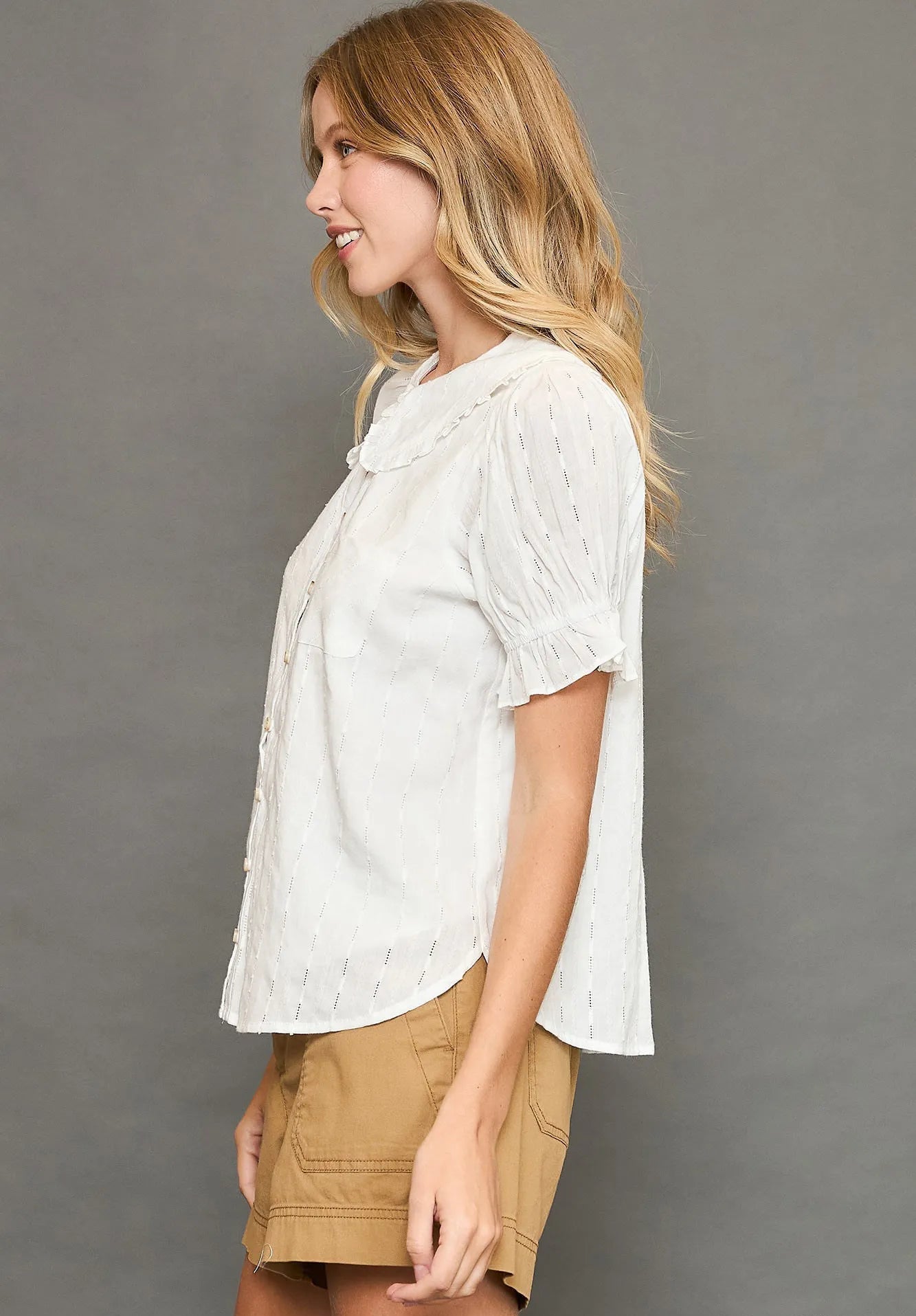 Woman wearing an off-white blouse and beige skirt against a gray background