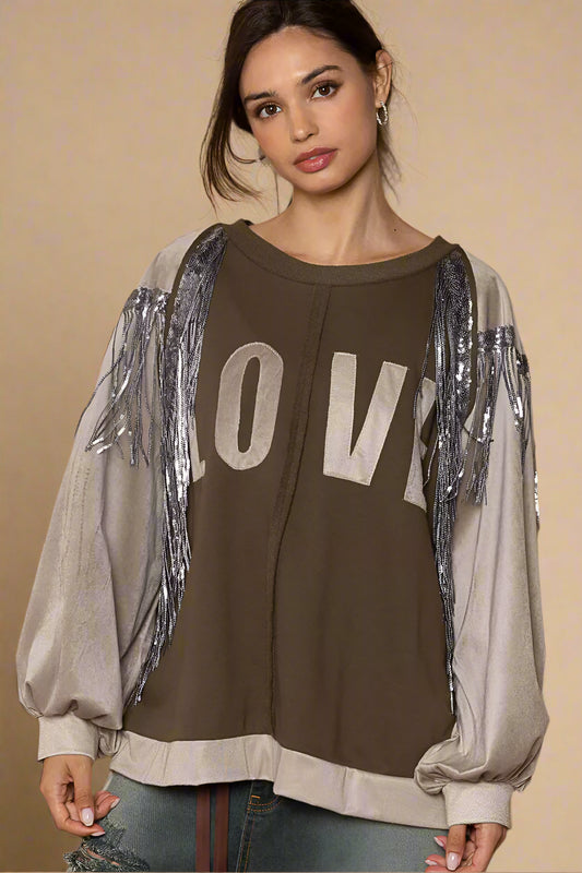 Woman wearing a brown sweatshirt with 'LOVE' print and silver fringe sleeves on a beige background