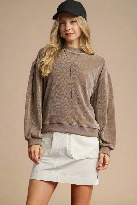 Woman wearing a brown sweatshirt and beige skirt against a red background