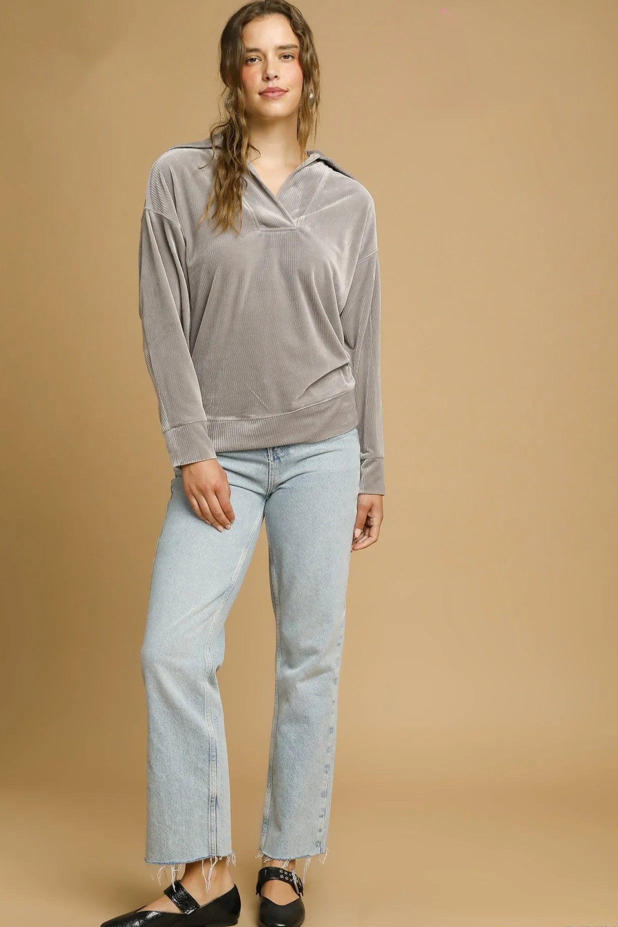Woman wearing a gray long-sleeve top and light blue jeans on a beige background