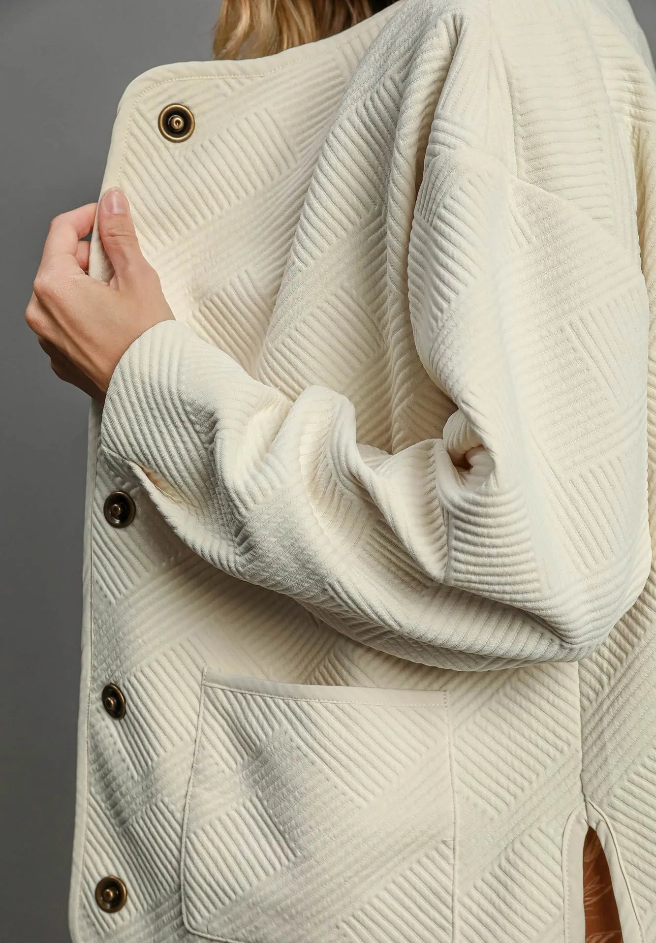 Close-up of a cream-colored textured coat with buttons on a gray background