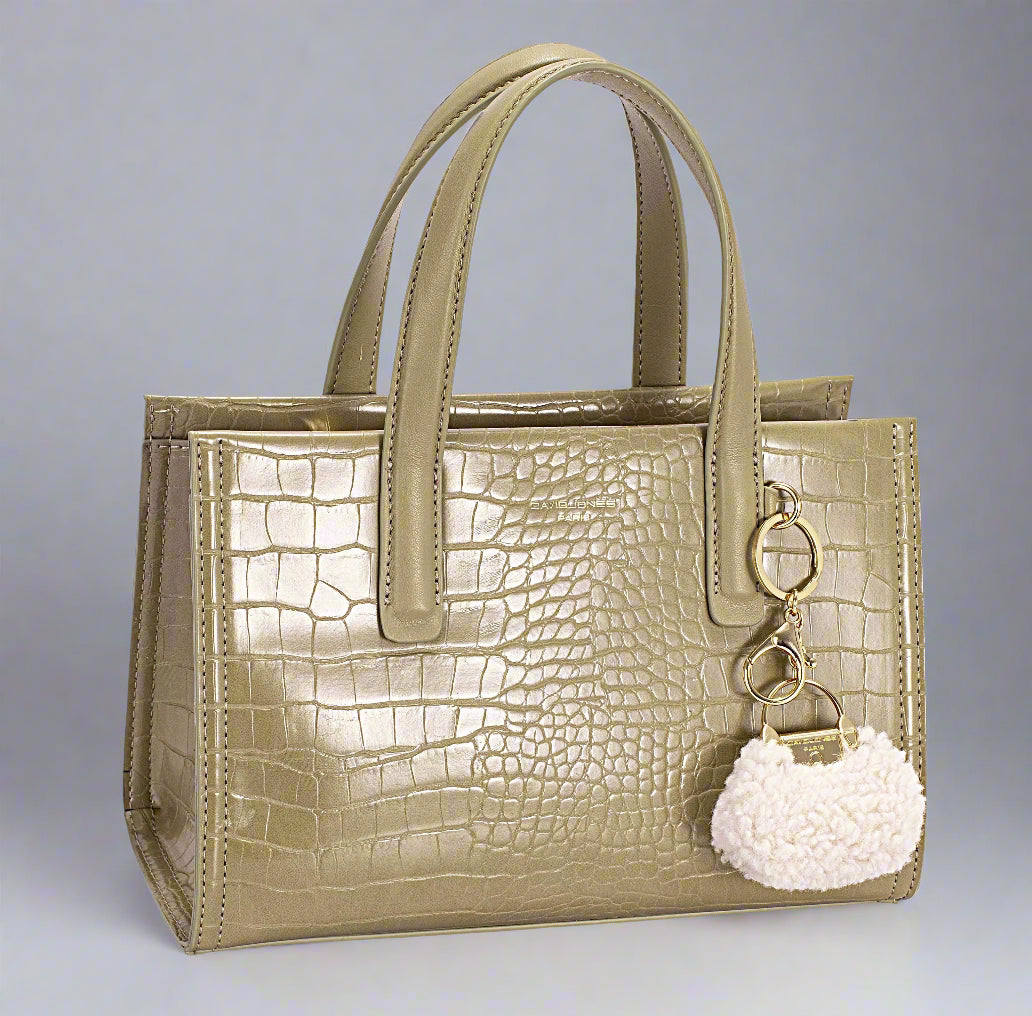 Beige crocodile-patterned handbag with a white pom-pom keychain on a white background