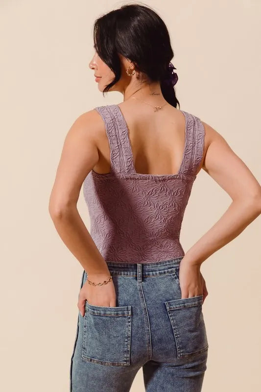 Woman wearing a textured brown tank top and blue jeans on a beige background
