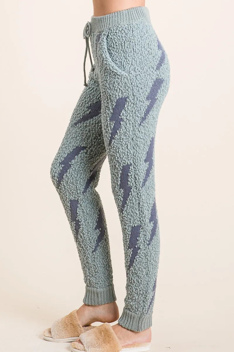 Light blue knitted jogger pants with dark blue lightning bolt pattern on a beige background