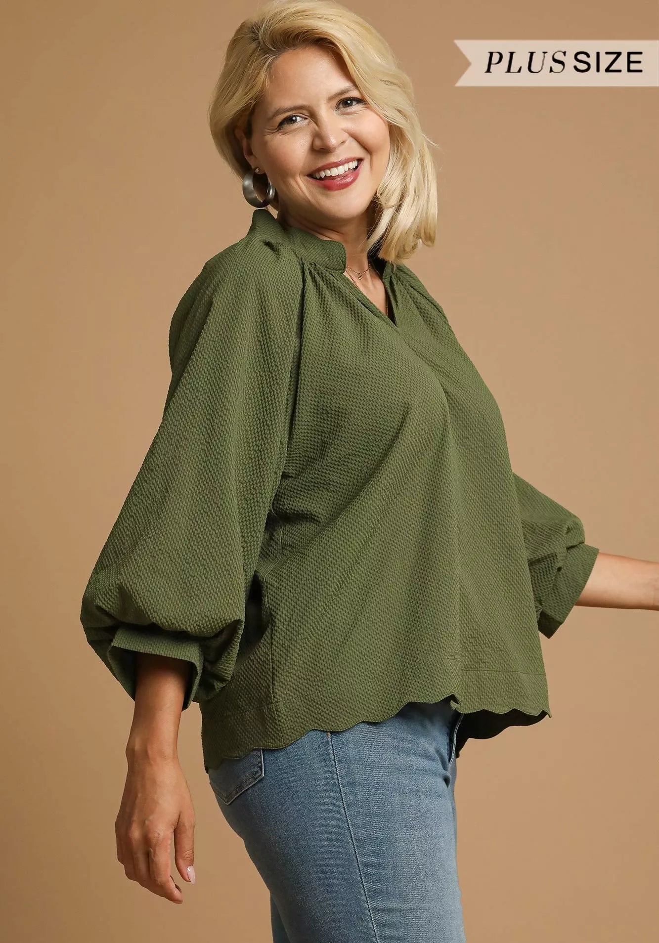 Woman wearing an olive green blouse and blue jeans on a beige background