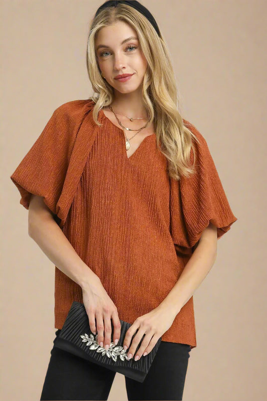 Woman wearing a rust-colored blouse holding a black clutch against a white background