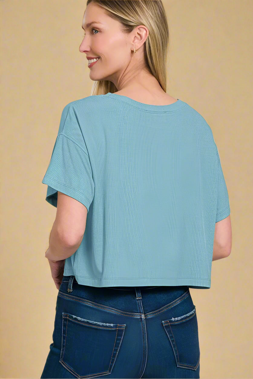 Woman wearing a dusty teal top and blue jeans on a white background