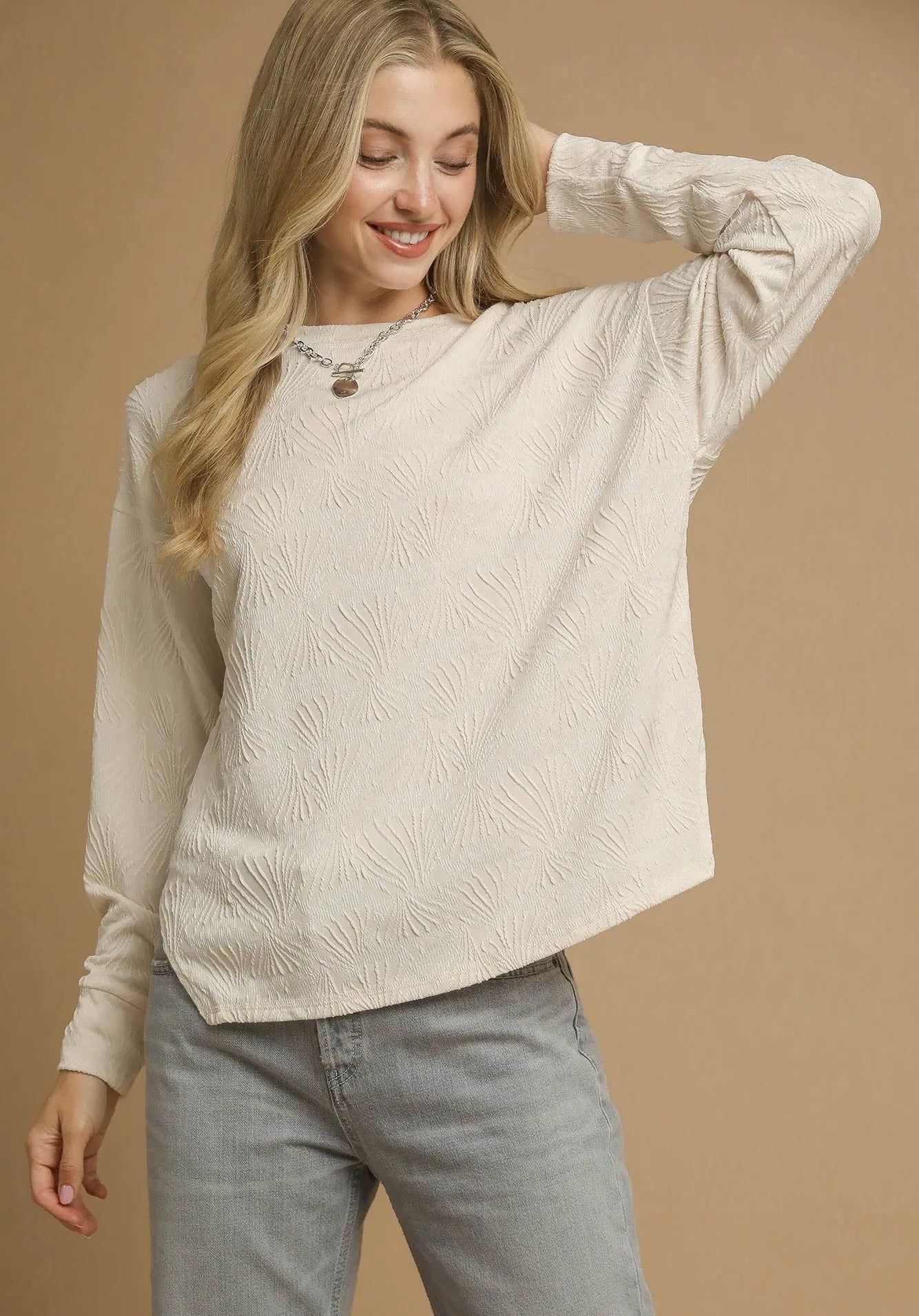 Woman wearing a beige sweater and gray pants against a beige background