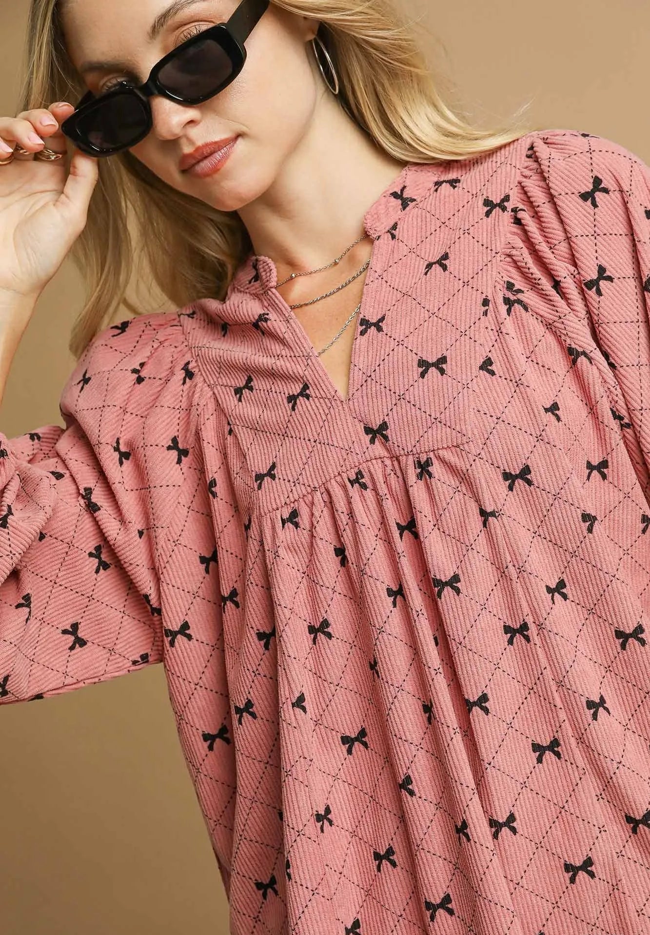 Woman wearing a pink blouse with black bow pattern against a beige background