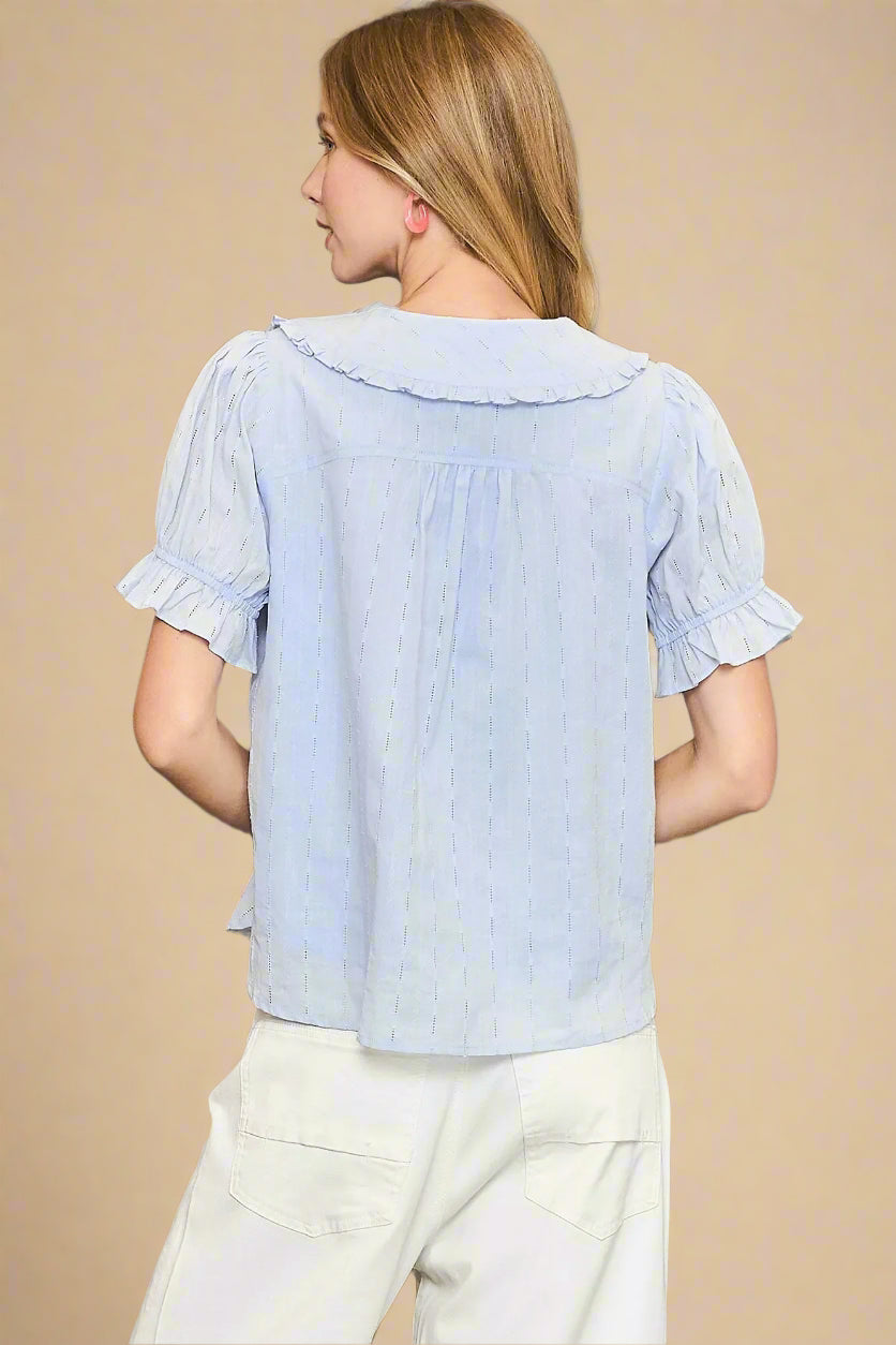 Woman wearing a light blue blouse with ruffled sleeves on a beige background