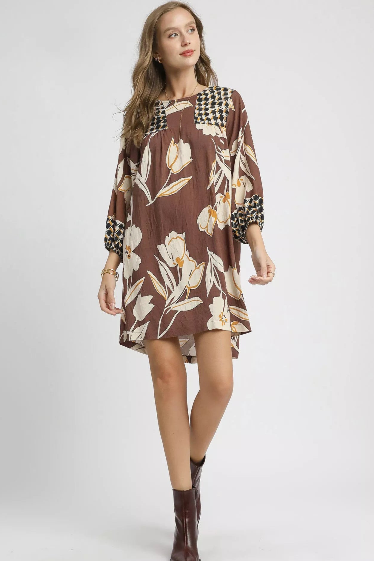 Woman wearing a brown floral dress with matching boots on a white background
