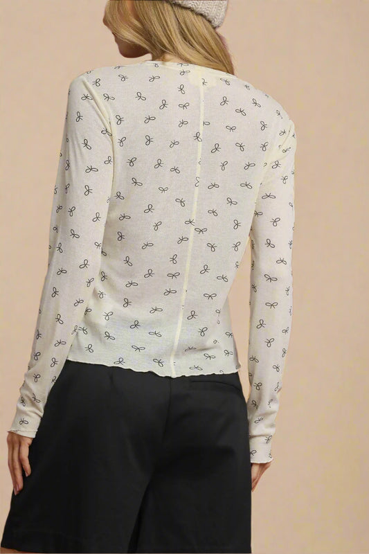 Person wearing a cream-colored blouse with black pattern on a beige background