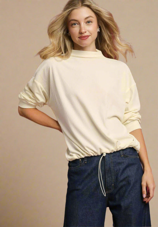 Woman wearing a beige sweater and blue jeans against a red background